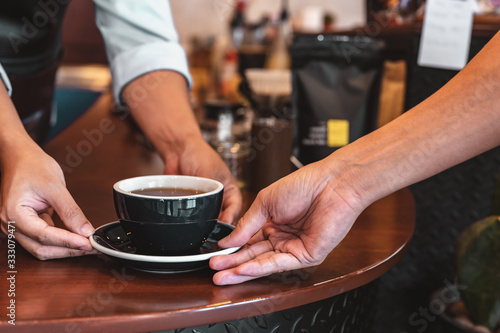 Close up of hands barista man serving coffee in coffee shop. male hands placing a cup of coffee on table. Coffee, Barista, extraction, serve, cafe, lifestyle concept.