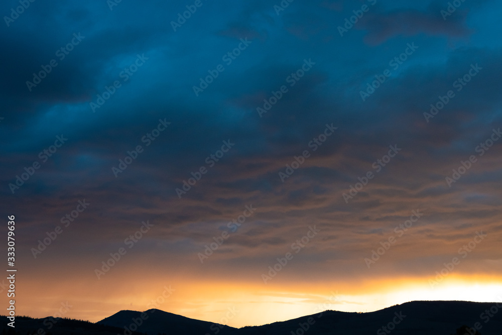 orange sunset and clouds over silhouette of mountain range