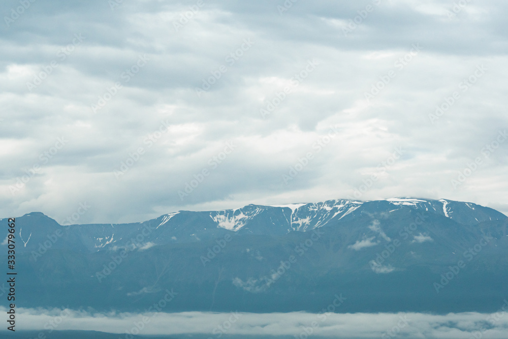 snow peaks on horizon, ridge of rocks under cloudy sky in mountain valley