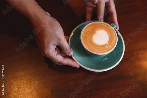 Close up of hands barista man serving coffee in coffee shop. male hands placing a cup of coffee on table. Coffee, Barista, extraction, serve, cafe, lifestyle concept.