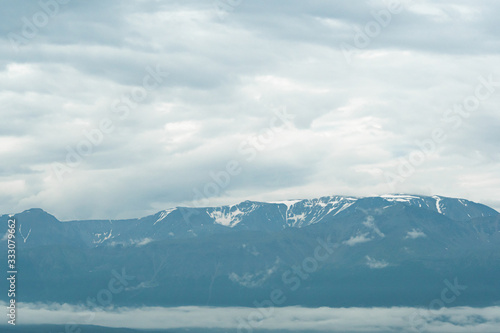 snow peaks on horizon, ridge of rocks under cloudy sky in mountain valley