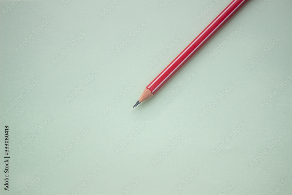 One red pencil on a light green background. One red pencil on a light green background.