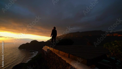 Man Standing At Cliff Edge Overlooking Sunset