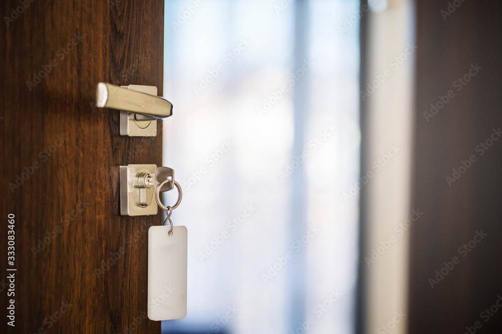 Close up on the half opened modern wooden Door handle with key in the lock of the empty hotel room or the apartment with blurred background in day