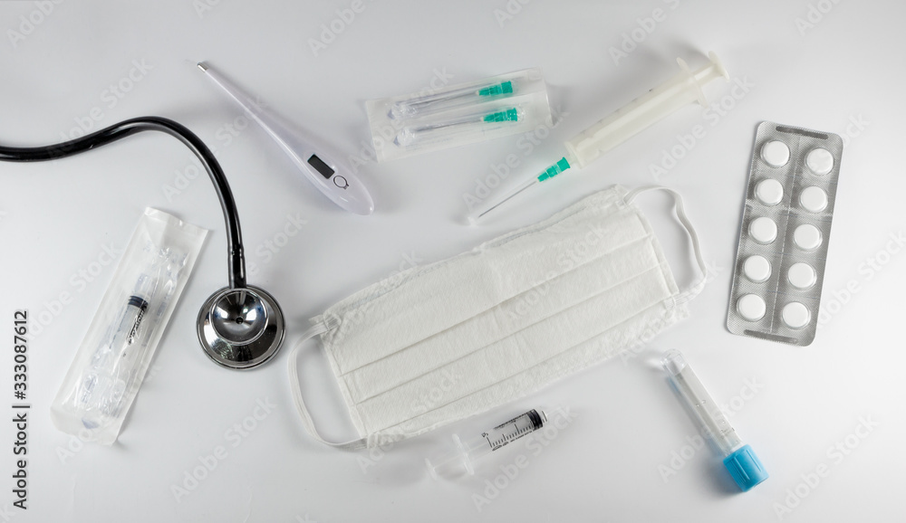 Fototapeta premium Medical equipment isolated on white background. Surgical protection face mask, syringes, needles, test tube, digital thermometer, pills and stethoscope. Corona Covid-19 protection concept, top view.