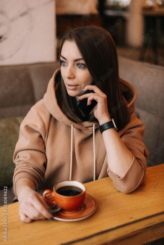 Attractive girl in a cafe at a table with a phone and a cup of coffee, talking on the phone. Concept of leisure activity. Attractive girl in a cafe at a table with a phone and a cup of coffee, talking on the phone. Concept of leisure activity.