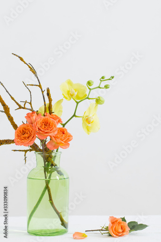 roses and orchids in green glass vase on white background