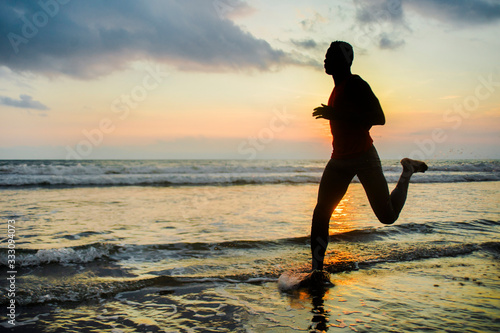 silhouette of young athletic and fit african american sport man doing running workout on sunset at the beach training hard jogging barefoot in healthy lifestyle concept