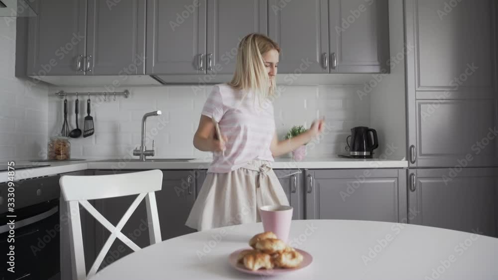 Young Excited Woman Holding Smartphone and Dancing In Kitchen. Young Excited Woman Holding Smartphone and Dancing In Kitchen.