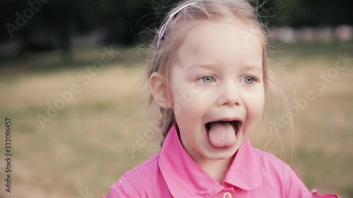 Beautiful little caucasian girl with big blue eyes, long fair hair, white skin smiles and shows her tongue