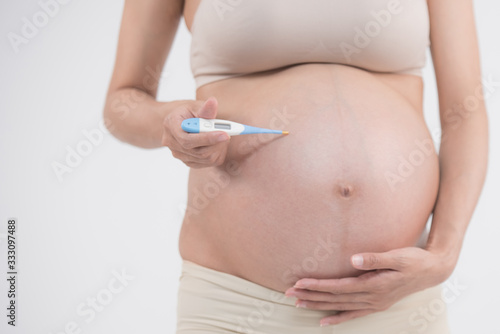 pregnant woman holding electronic thermometer with normal temperature. health during pregnancy. pregnancy illness. young pregnant woman feeling sick with high fever. concept healthy care pregnancy..