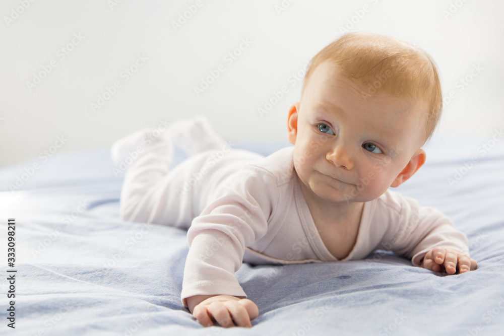 Positive adorable blue eyed baby girl crawling on parents bed. Six month child lying on belly at home. Childhood or baby care concept Positive adorable blue eyed baby girl crawling on parents bed. Six month child lying on belly at home. Childhood or baby care concept