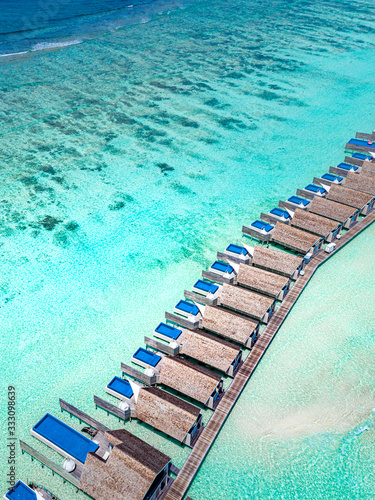 The drone photo with a wooden water villas seen from above and an amazing blue lagoon crystal clear water close to tropical lagoon. Amazing summer travel and vacation background. Dreamy beach scenery