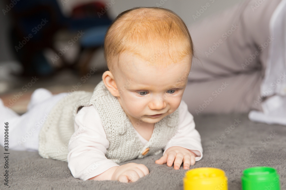 Focused cute red haired baby girl playing learning game with toys. Six month child crawling on grey carpet on floor. Childhood or baby care concept Focused cute red haired baby girl playing learning game with toys. Six month child crawling on grey carpet on floor. Childhood or baby care concept