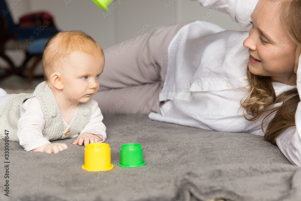 Happy new mom and baby daughter playing learning game on floor. Young woman and six month child enjoying leisure time at home. Motherhood concept Happy new mom and baby daughter playing learning game on floor. Young woman and six month child enjoying leisure time at home. Motherhood concept