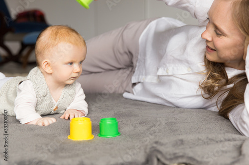 Happy new mom and baby daughter playing learning game on floor. Young woman and six month child enjoying leisure time at home. Motherhood concept
