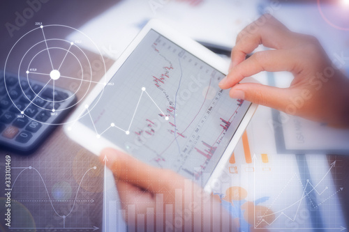 Trader using tablet with financial analysis graphs. Closeup of person working with candlestick chart. Papers and calculator lying on desk. Trading and FOREX concept. Cropped view.