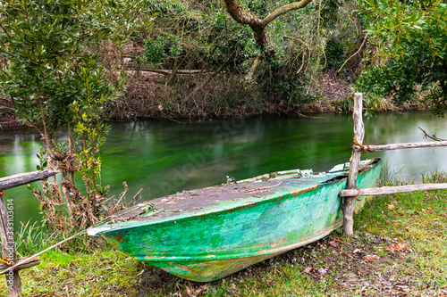 Vecchia barca di colore verde ormeggiata lungo il torrente Corgnolizza. Vegetazione spontanea.  photo