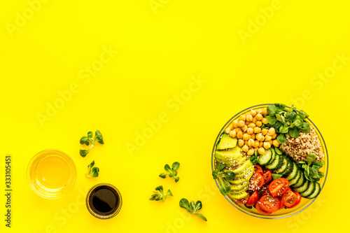 Healthy salad bowl with quinoa, avocado and chickpeas on yellow background top-down copy space