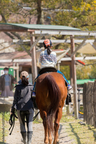 春の牧場で乗馬体験している可愛い子供