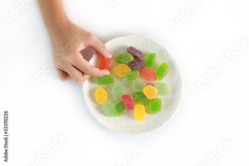 Top view hand of kid holding a gummy sugary candy from a white plate