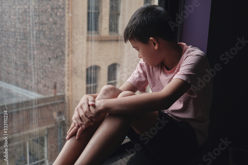 Photography Sad Asian preteen boy feeling lonely, looking out of window from his room, socia