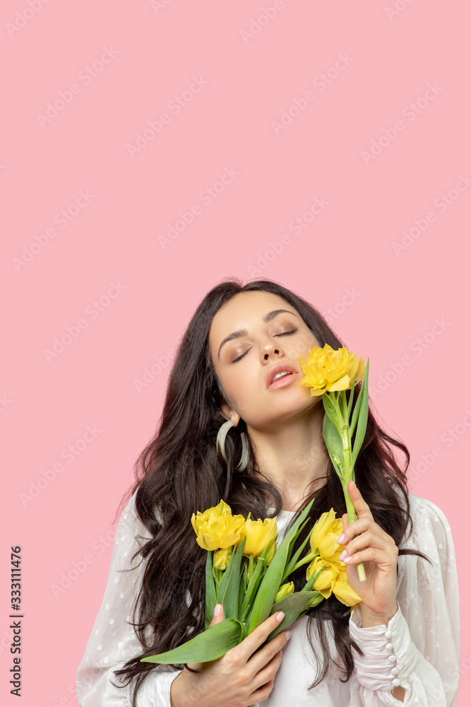 Young pretty dark-haired woman holding yellow flowers and looking relaxed Young pretty dark-haired woman holding yellow flowers and looking relaxed