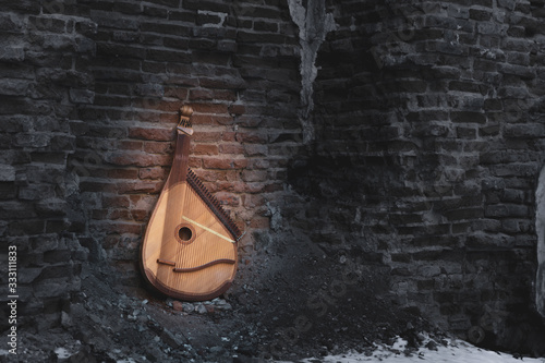 A tree-colored bandura next to the arch in a stone black-and-white wall on snowy ground, an ancient national Ukrainian instrument, archetypal, spiritual, vintage photo with a bright accen