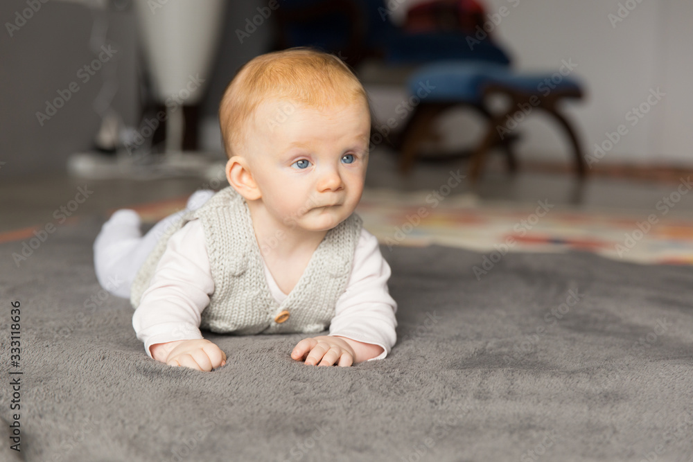 Beautiful blue eyed baby girl crawling on carpet at home. Six month child lying on belly on floor. Childhood or baby care concept Beautiful blue eyed baby girl crawling on carpet at home. Six month child lying on belly on floor. Childhood or baby care concept