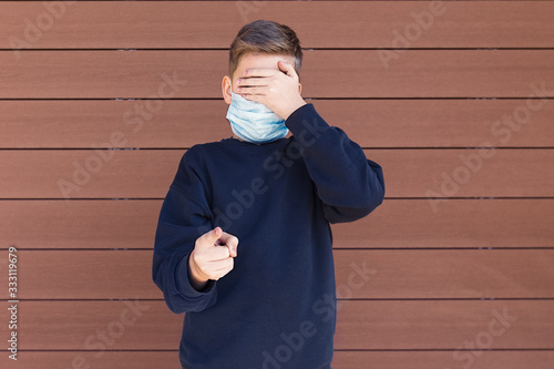 Obraz na płótnie A boy standing outside with protection face mask shields eyes with his hand and points his finger w salonie