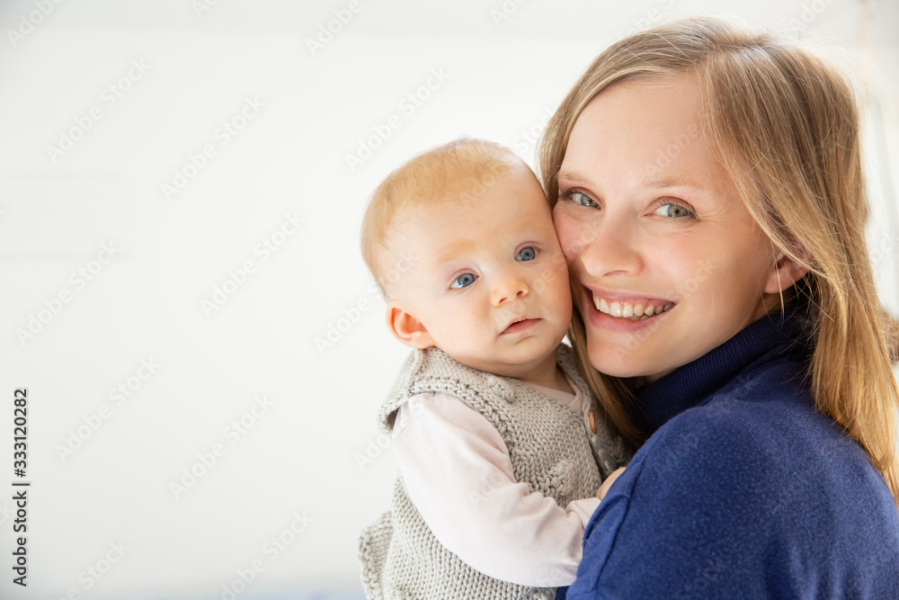 Happy mother and infant daughter smiling at camera. Portrait of happy young mother holding adorable infant baby girl isolated on white background. Parenthood concept Happy mother and infant daughter smiling at camera. Portrait of happy young mother holding adorable infant baby girl isolated on white background. Parenthood concept