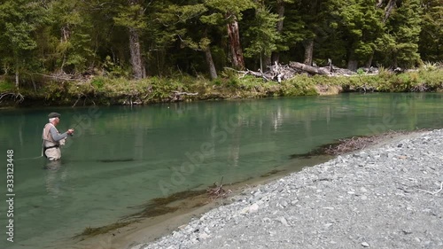 Fly fisherman wading in a clear river and casting his nymph upstream. Dense rainforest on the riverbank behind. Eglinton River, Fiordland National Park, Southland, New Zealand. photo