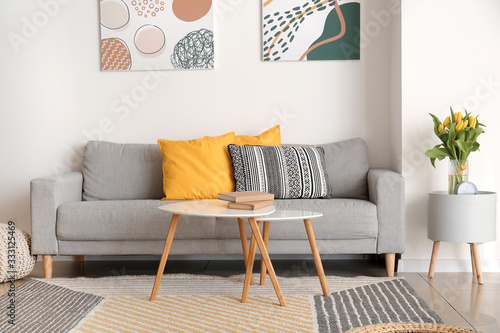 Interior of modern room with comfortable sofa and table with spring flowers