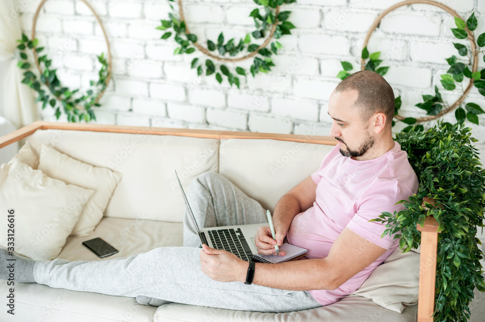 Naklejka premium Man using laptop and taking notes at home