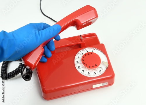 A male hand in a rubber glove holds a telephone receiver in the hand of a vintage red landline phone on a white background. Classic red telephone.The concept of a commercial cleaning company.