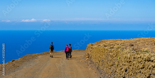 Hikers walked along a wide path on the Island of El Hierro. The horizon line of the Atlantic Ocean is observed.