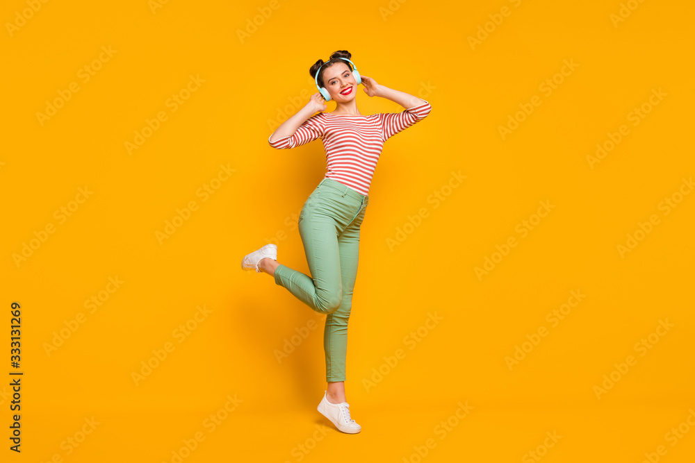 Full length profile photo of pretty lady enjoy warm spring day traveling listen earphones wear casual red white shirt green pants sneakers isolated bright yellow color background