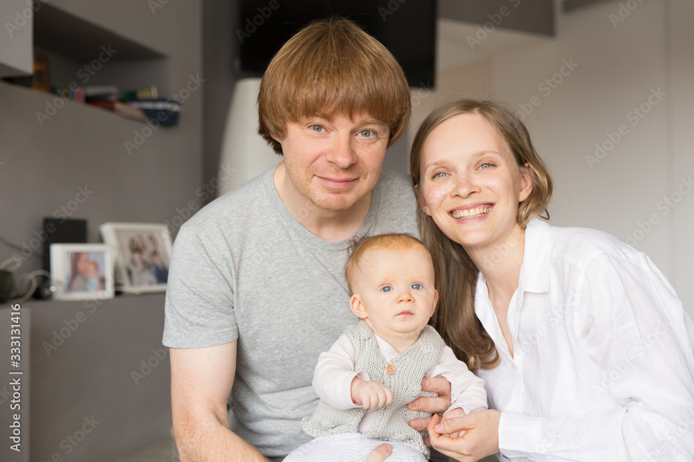 Joyful positive new parents holding baby daughter. Young couple holding six month child and looking at camera. Parenthood concept