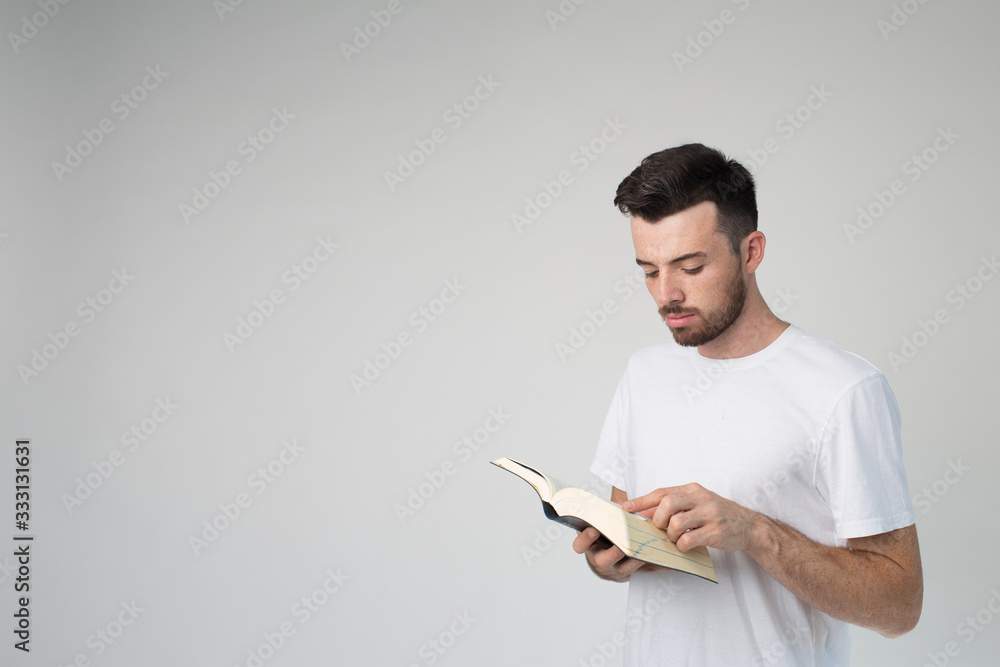 Young man isolated over background. Side view of guy reading book and standing in room alone. Point with finger. Smart wise young man on picture. Young man isolated over background. Side view of guy reading book and standing in room alone. Point with finger. Smart wise young man on picture.