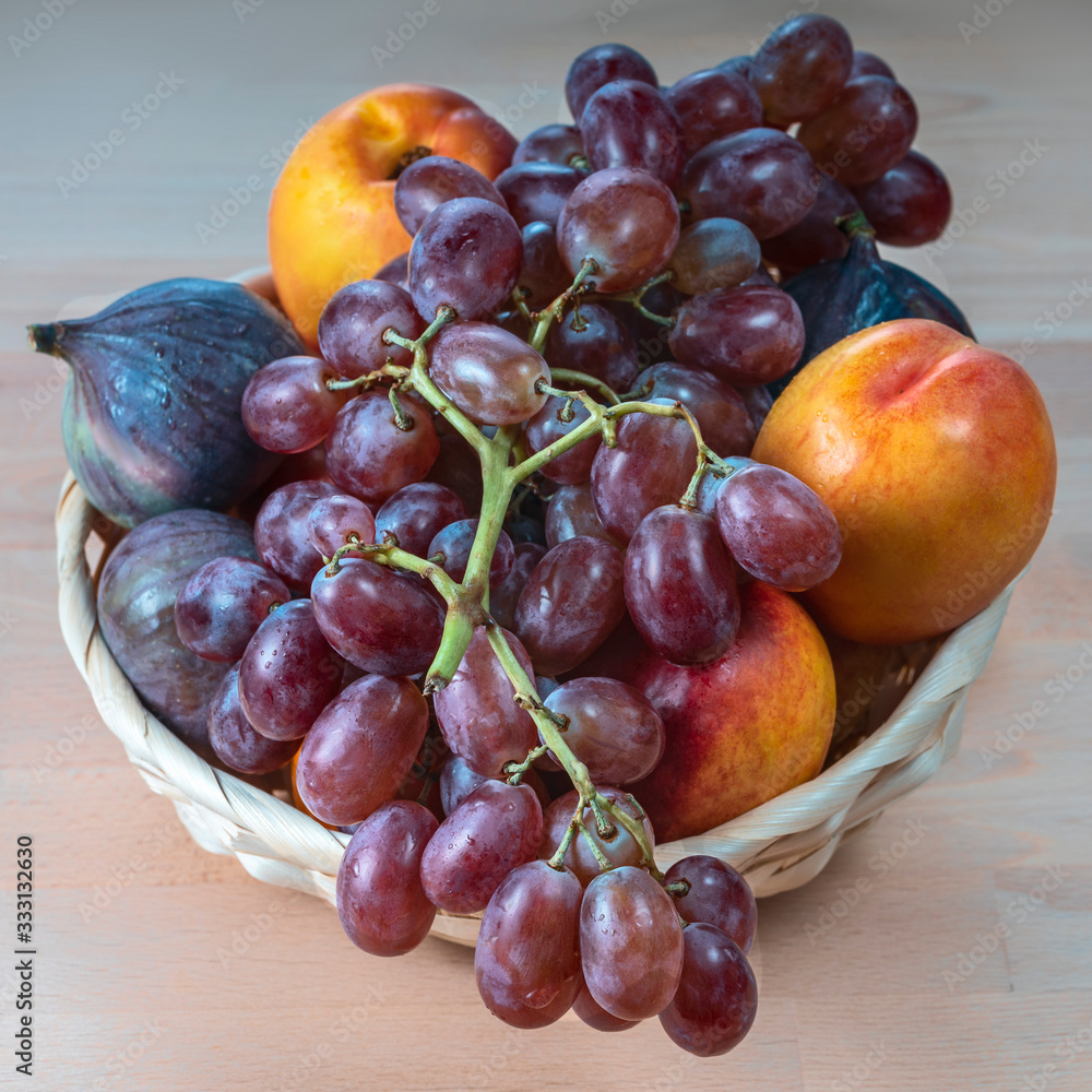 Fototapeta premium red grapes and fresh fruits in a straw basket on a light kitchen table