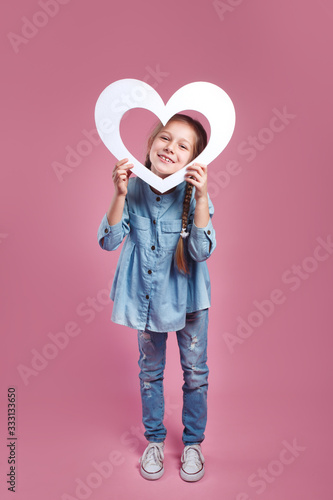 Funny little girl looking through a heart shape on pink background