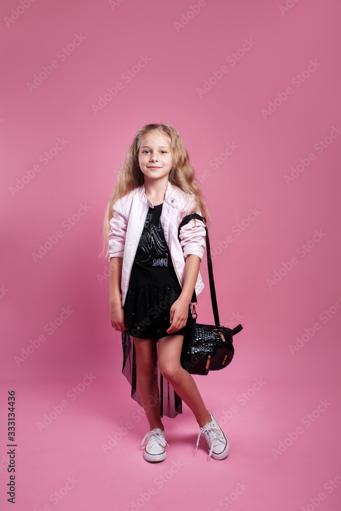 fashionable little girl wearing black dress and pink leather jacket posing on pink studio background