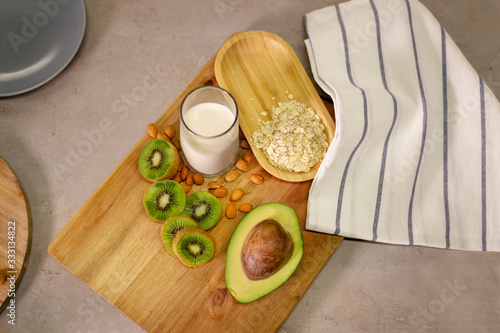 Half an avocado, slices of kiwi, almond, oats and milk on a board covered with a kitchen towel. Ingredients for a nutritious and healthy tasty breakfast.