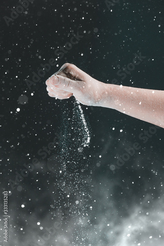 On a black background  a woman s hand pours white flour like snow for baking