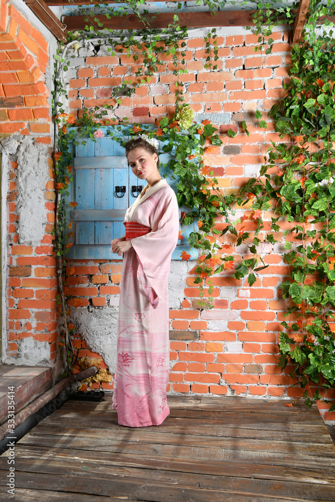 girl in japanese kimono posing on the background of flowering plants girl in japanese kimono posing on the background of flowering plants