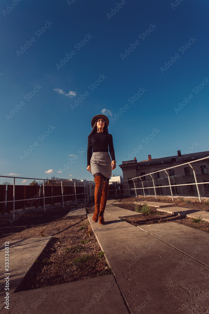 Young pretty stylish girl walking along the street. Girl model in hat walks along the street.