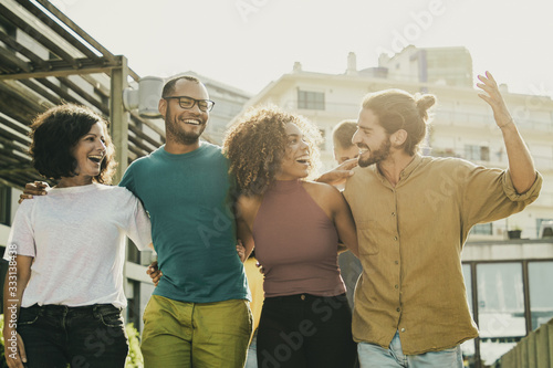 Content friends embracing and walking outdoors. Happy multiethnic friends walking and talking together on street. Friendship concept