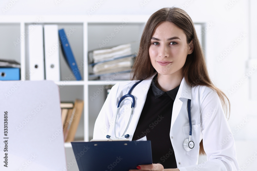 Beautiful smiling female doctor hold clipboard pad and fill something with silver pen. Physical, illness prevention, prescribe remedy, ward round, therapeutist assistance, healthy lifestyle concept Beautiful smiling female doctor hold clipboard pad and fill something with silver pen. Physical, illness prevention, prescribe remedy, ward round, therapeutist assistance, healthy lifestyle concept
