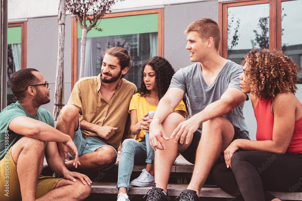 Young friends sitting on steps. Cheerful young multiethnic men and women sitting together on street and interacting. Friendship concept Young friends sitting on steps. Cheerful young multiethnic men and women sitting together on street and interacting. Friendship concept