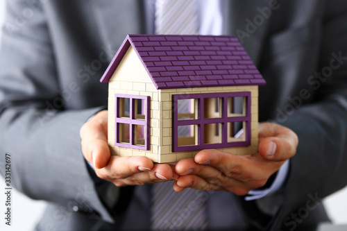 Man in suit and tie cover with arms little toy house closeup. Palm shelter, save and trust, defende owner wealth, sell or rental structure, loan idea, no problems, buy defence, future plan concept